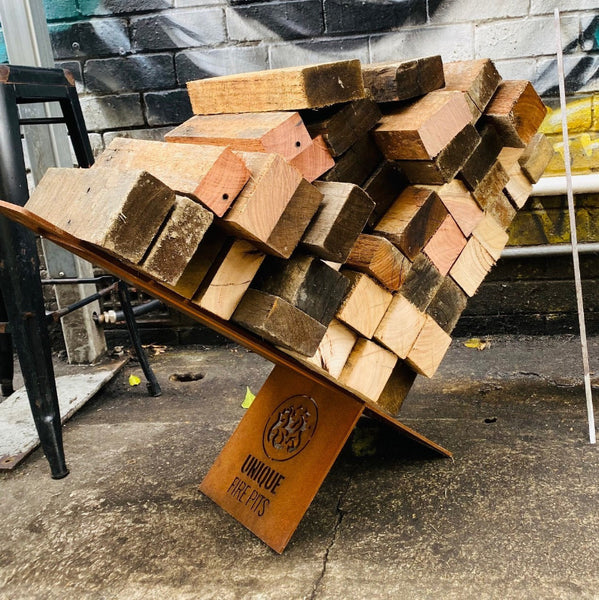 Stack of firewood on a metal stand with 'UNIQUE FIRE FITS' branding against a brick wall.