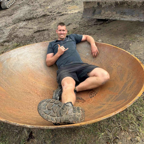 Young man laid back and relaxing inside the Crucible Fire Pit with muddy area surround and construction diggers.