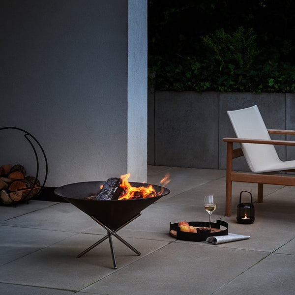Outdoor patio with cone shaped fire pit, an outdoor chair, and wine glass with nibbles on a dark evening.