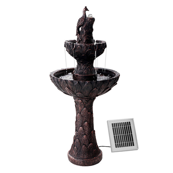 A brown, three-tier solar-powered water fountain featuring a peacock at the top, with a solar panel attached to its base set on a white background.