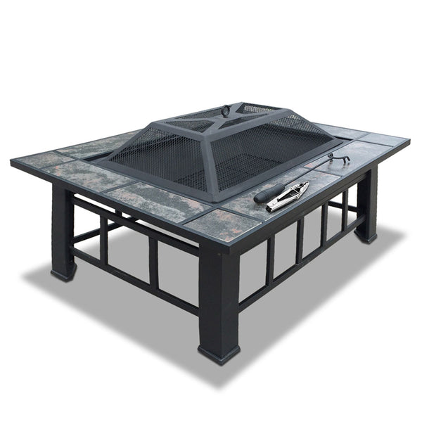 A 3-in-1 steel fire pit/BBQ grill outdoor table with grey tiles on the tabletop and a mesh dome on top with a poker and tongs set in a white background.