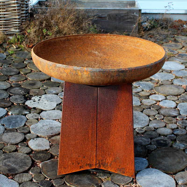 Yagoona Goanna Outdoor Fire Pit Australia in rust with a log wood flooring, a wooden box, weeds and cane basket in the background.