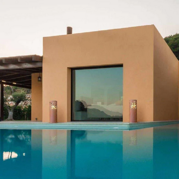 Gustav Commerce Corten Finish Outdoor Fireplaces outside near a swimming pool with a house and garden in the background.