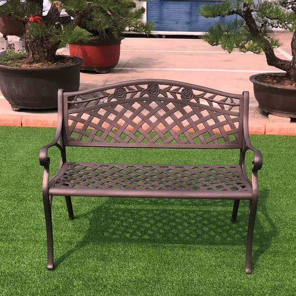 Melissa Cast Aluminium Bench in a garden setting on grass area in front of large tiled patio area with large garden pots and bonsai trees.