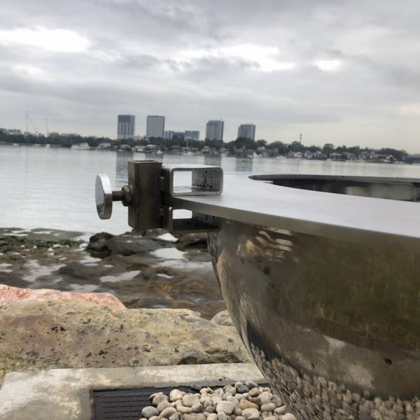 Teppanyaki Spit Rotisserie Bracket on side of the fire pit beside a body of water, buildings and boats in the background