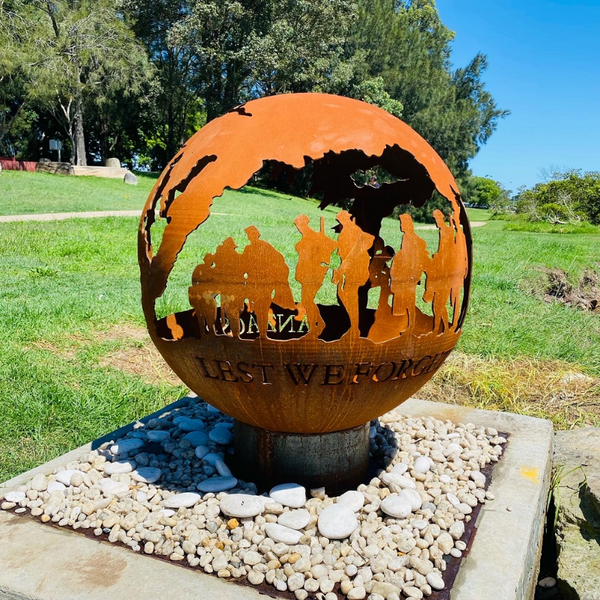 The Anzacs Fire Pit with soldiers design and the words Lest we Forget cut in it. Sitting on a gravel surround with lawn and trees around in the backdrop.