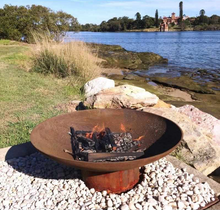 Load image into Gallery viewer, The Cauldron Cast Iron Fire Pit in rust with a small fire burning