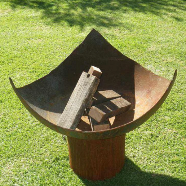 The Chalice Fire Pit with wood stacked inside it and set up on a lovely green lawn