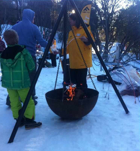 The Tripod Fire Pit in the snow with people close by toasting marshmellows