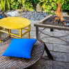 Outdoor setting with a yellow table, wicker chair with a blue cushion, and fire pit.
