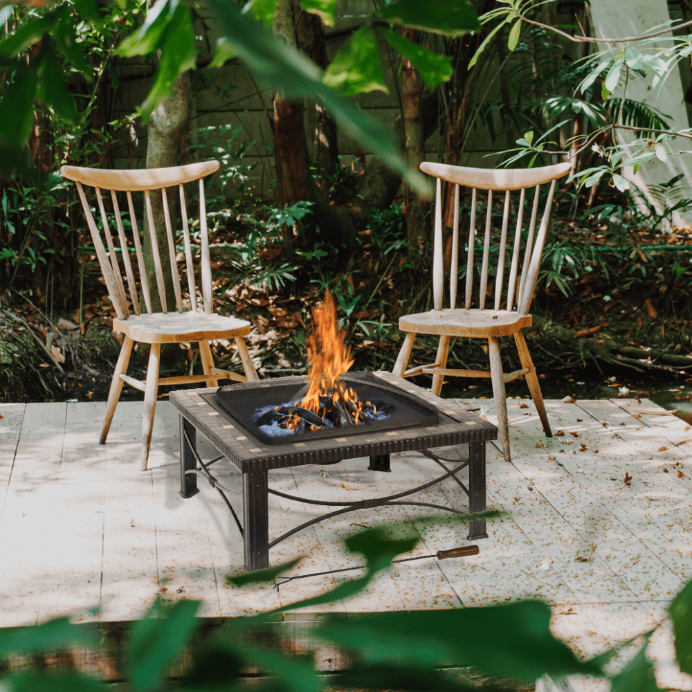 Two wooden chairs around a fire pit on a patio with greenery in the background