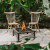 Two wooden chairs around a fire pit on a patio with greenery in the background