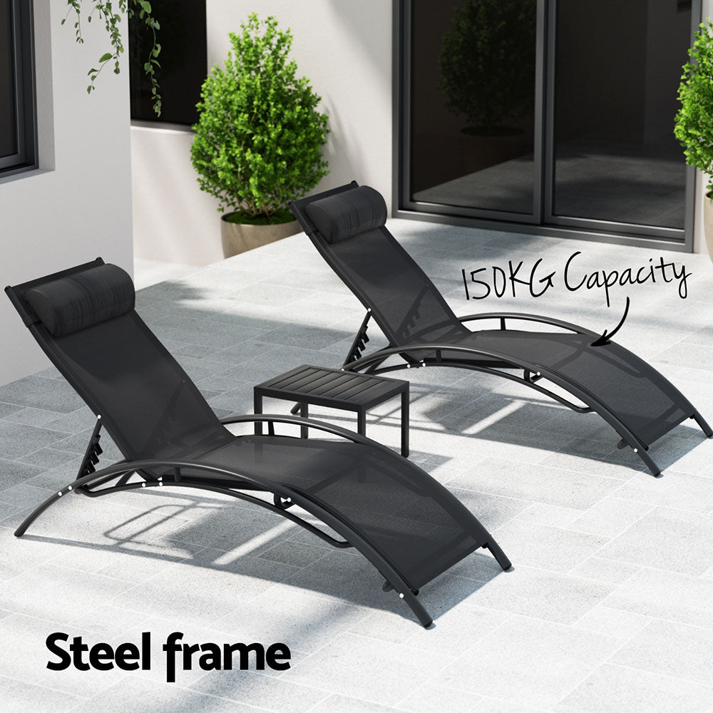 Two black Gardeon sun loungers with adjustable backrests and a small steel table showing the weight capacity of chairs as 150kg, set on a tiled patio outside a house with couple of trees potted in large pots.