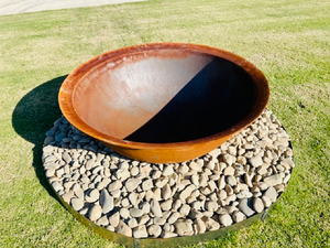 The Crucible Fire Pit sitting on river rocks in a lawn area