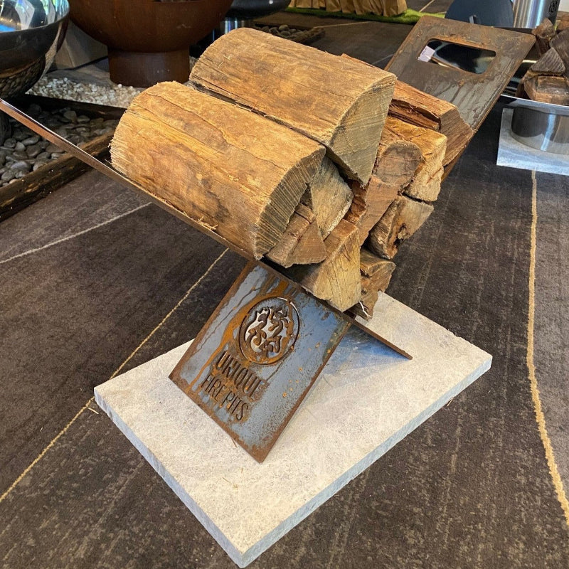 Wooden firewood stack on a metal stand with 'Unique Fire Pits' branding on a stone surface.