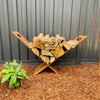 Metal firewood rack with stacked logs against a grey fence wall.
