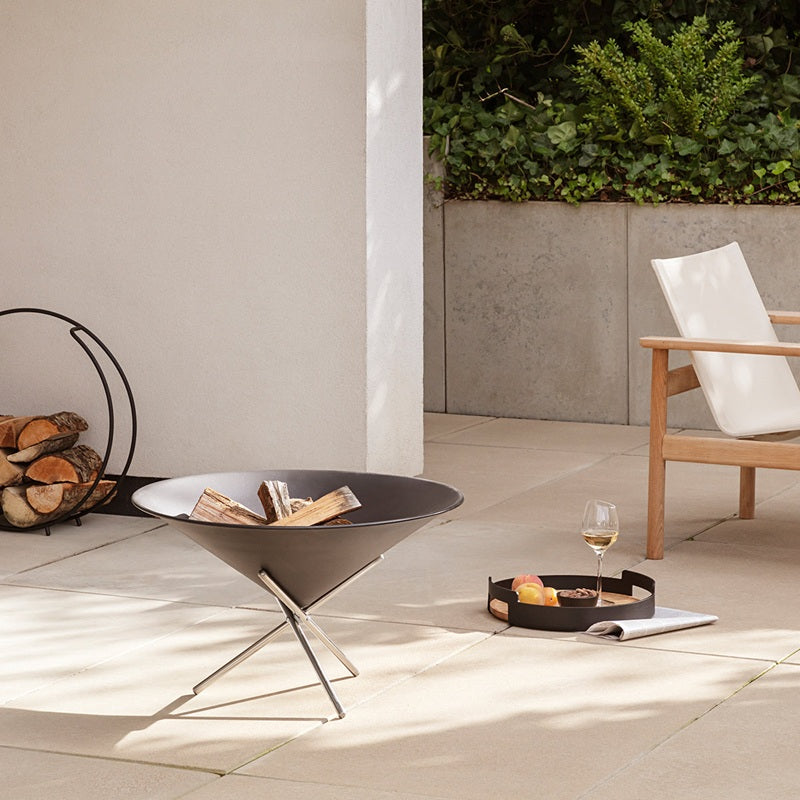 Outdoor patio setting with a chair, firepit, log rack and decorative items on a tiled floor.