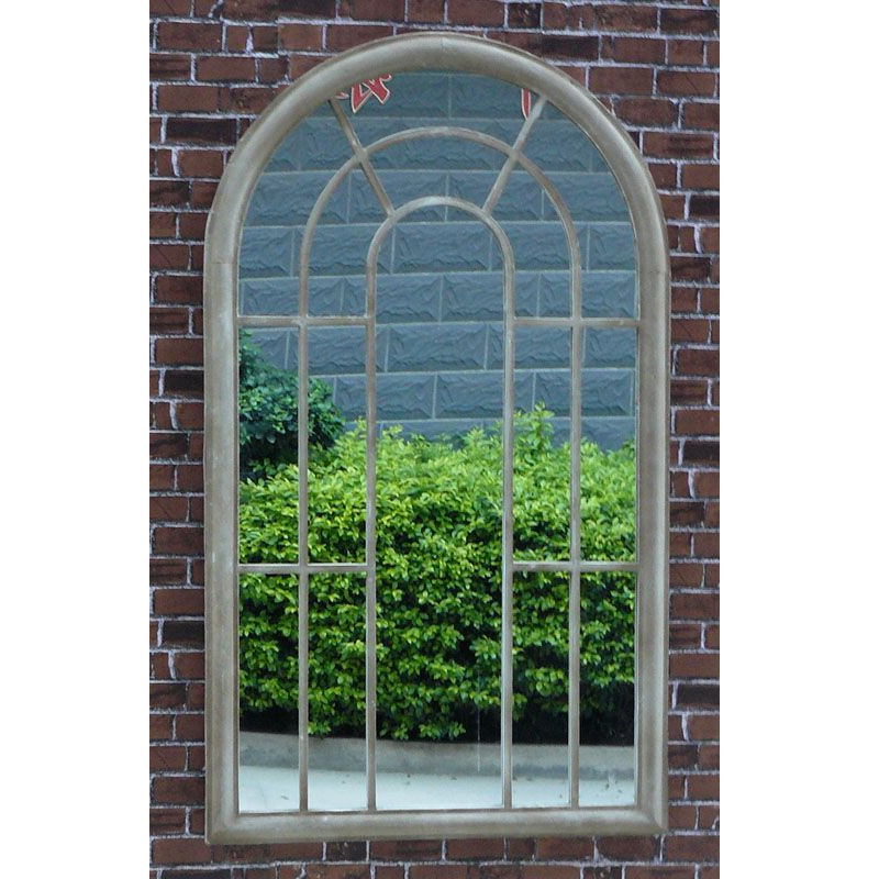 Tracey Garden Window Mirror on an outside brick wall with garden hedges in the mirror's reflection.
