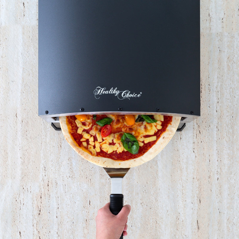 Pizza being cooked on a portable pizza oven labeled 'Healthy Choice' against a light stone wall.