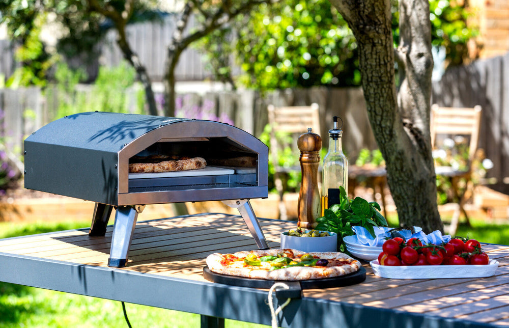 Outdoor pizza oven with a pizza on a table in a garden setting