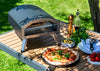 Outdoor pizza oven with a pizza on a wooden table outdoors.