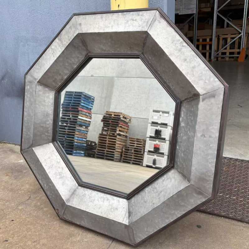 Viking Octagonal shaped Metal Mirror on cement floor and leaning on a wall in a warehouse with a few piles of stacked wooden pallets showing in the reflection of the mirror.
