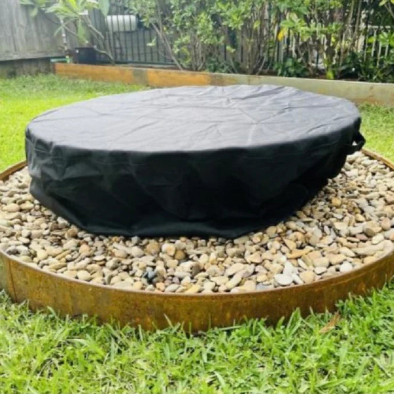 A fire pit on a pebble surface with a vinyl cover in a garden setting.