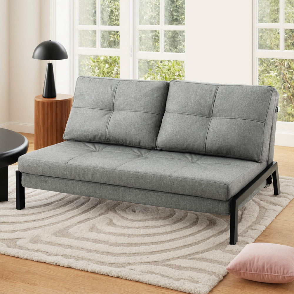 Gray sofa bed in a living room setting with a lamp and rug.