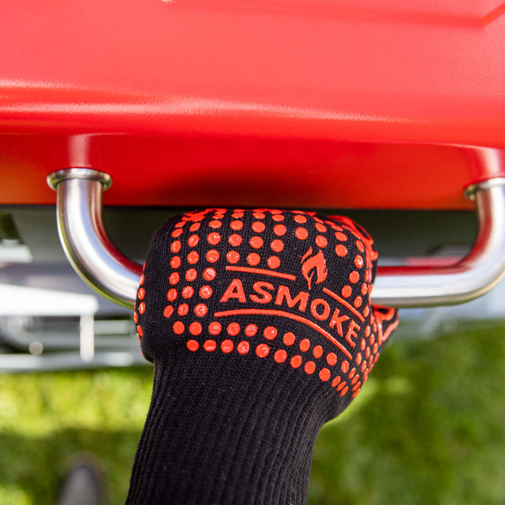 Black glove with red text holding onto a red barbecue grill handle.