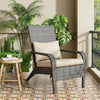 Gray wicker chair with beige cushion on a balcony with plants and a small table.