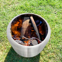 Looking down into a cylindrical stainless steel fire pit with a fire burning on a green grass surface.