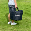 Someone carrying a large black carry bag with the word's bonfire pit and a logo on it, on a green grass area.