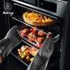 Person wearing oven mitts opening an oven with various dishes inside, including a pie and stuffed peppers.