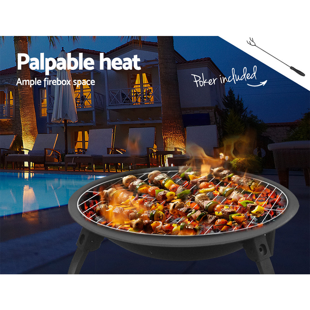 A portable black fire pit with a foldable design, cooking meat and vegetable kebabs, set next to a poolside with chairs around and a house in the background.