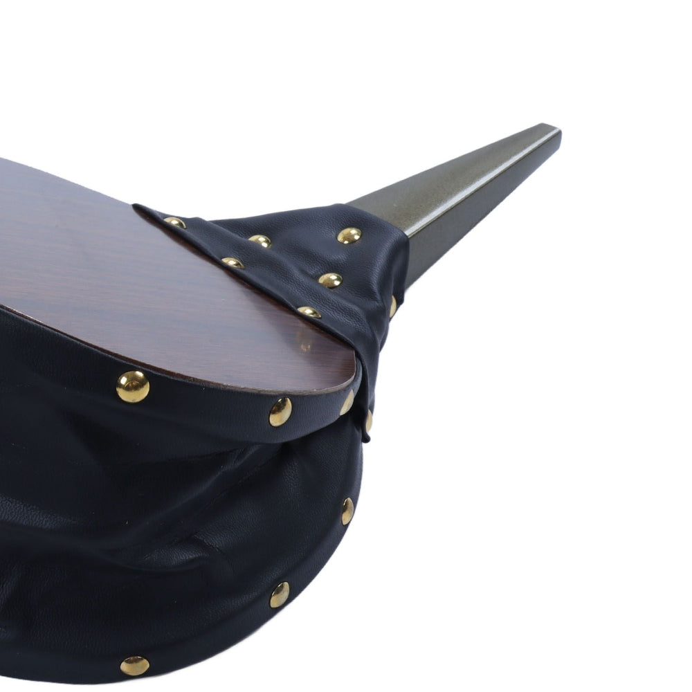 Close-up of a black draped fabric accessory with gold-tone metal studs and a dark wood-grain top surface, shown against a plain white background.