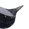 Close-up of a black draped fabric accessory with gold-tone metal studs and a dark wood-grain top surface, shown against a plain white background.