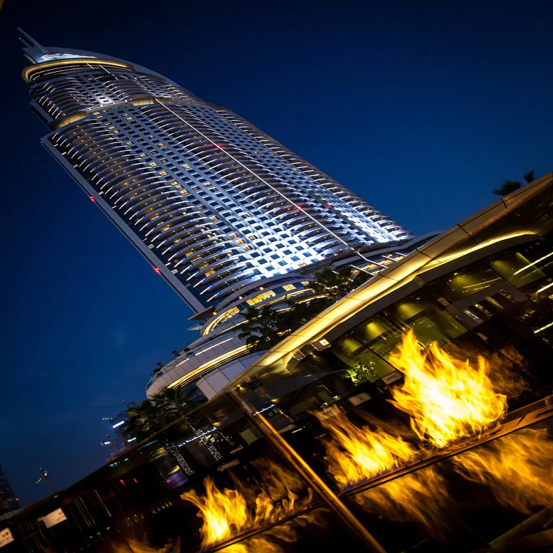 Galio Gas Fire Pit Insert Linear Automatic with fire burning at nighttime at a poolside and upwards view of a really tall highrise building in the background.