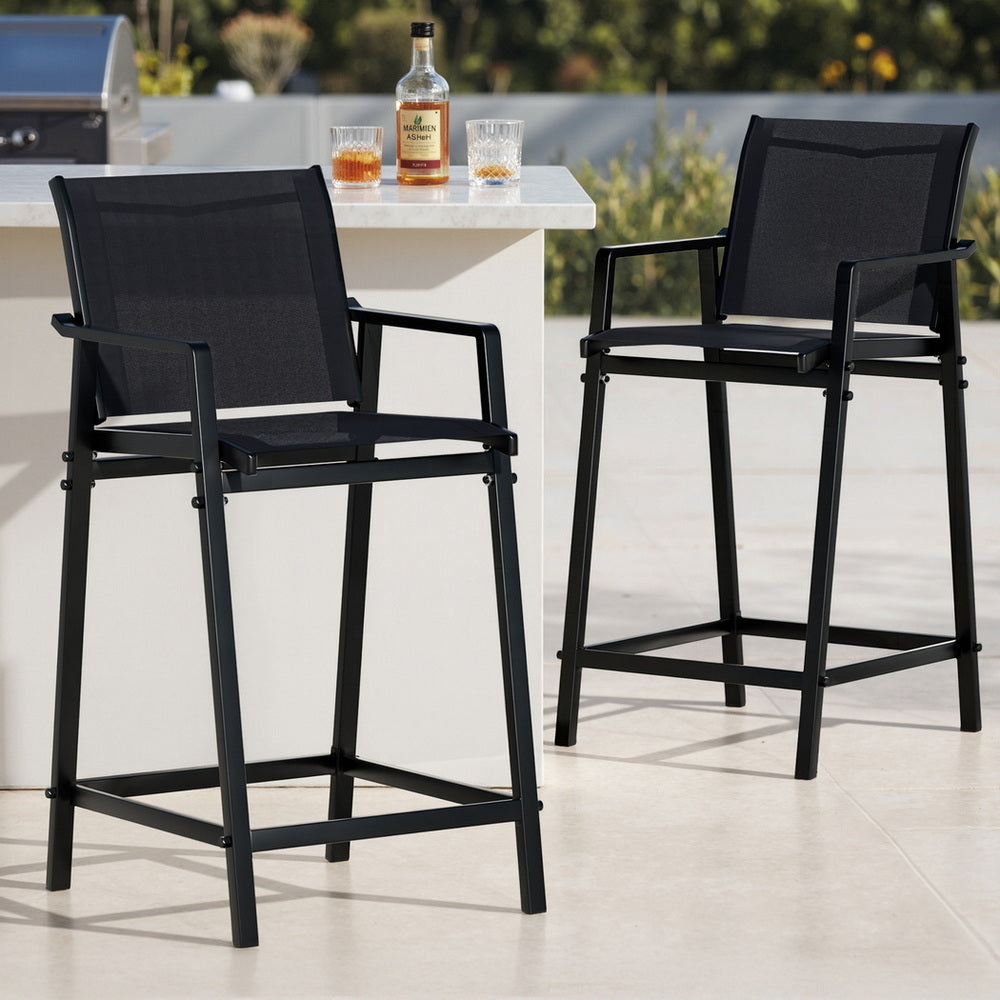 Two black outdoor bar stools with a table featuring a bottle and glasses on a patio.
