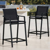 Two black outdoor bar stools with a table featuring a bottle and glasses on a patio.