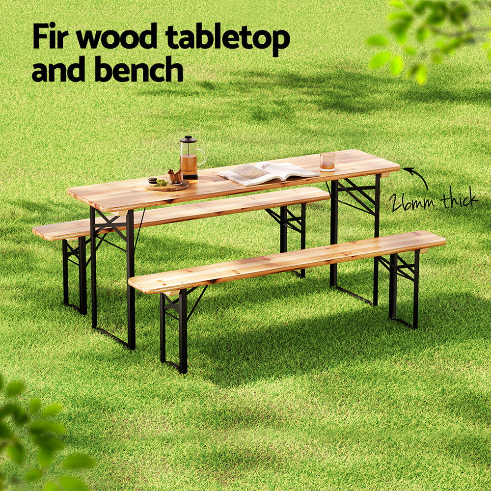 A set of outdoor furniture consisting of a wooden tabletop with an open book, a teapot and glass of tea and plate of food, and two matching benches with black metal frames and set on a green grass area.