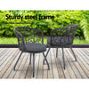 Two black rattan chairs with black cushions on a black frame, set on a wooden decking in front of a grass and greenery in the backdrop.