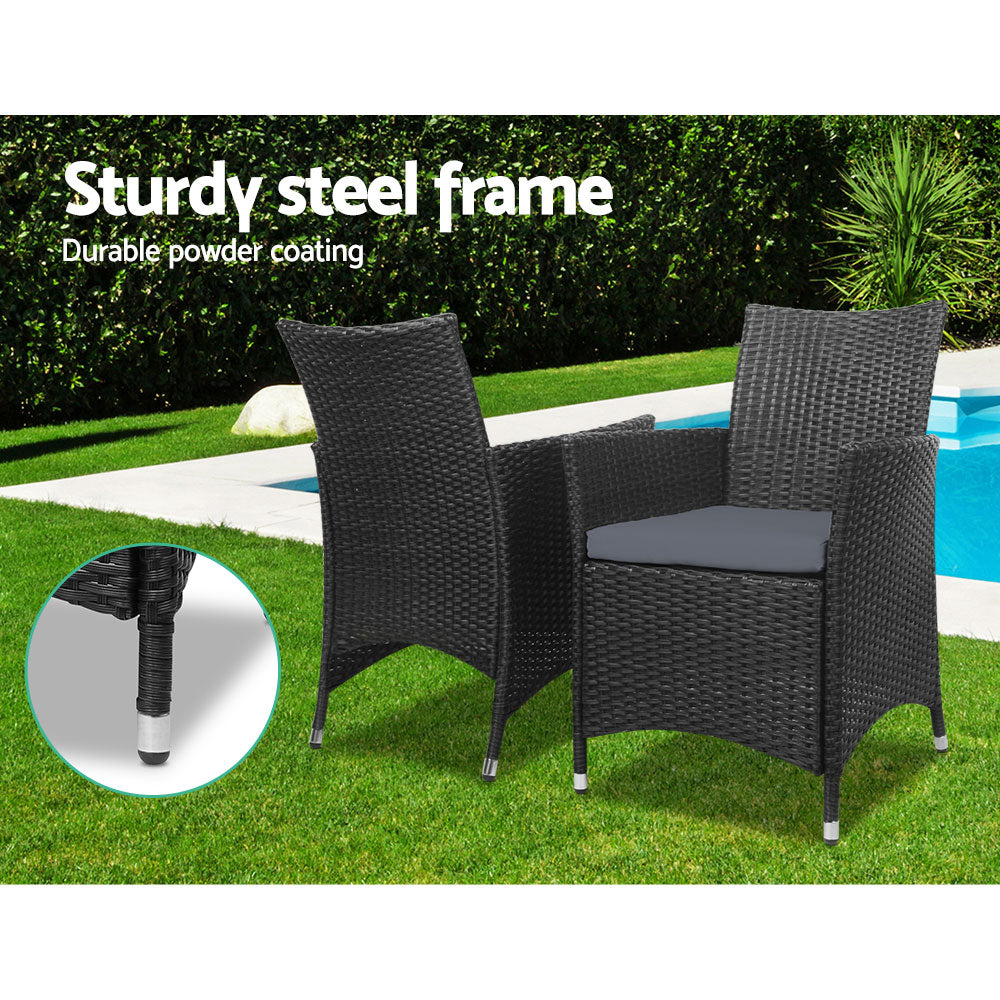 Two black wicker chairs with cushions on a green lawn, beside a pool with tree hedging in the background, an inserted image showing close-up of the chair leg.