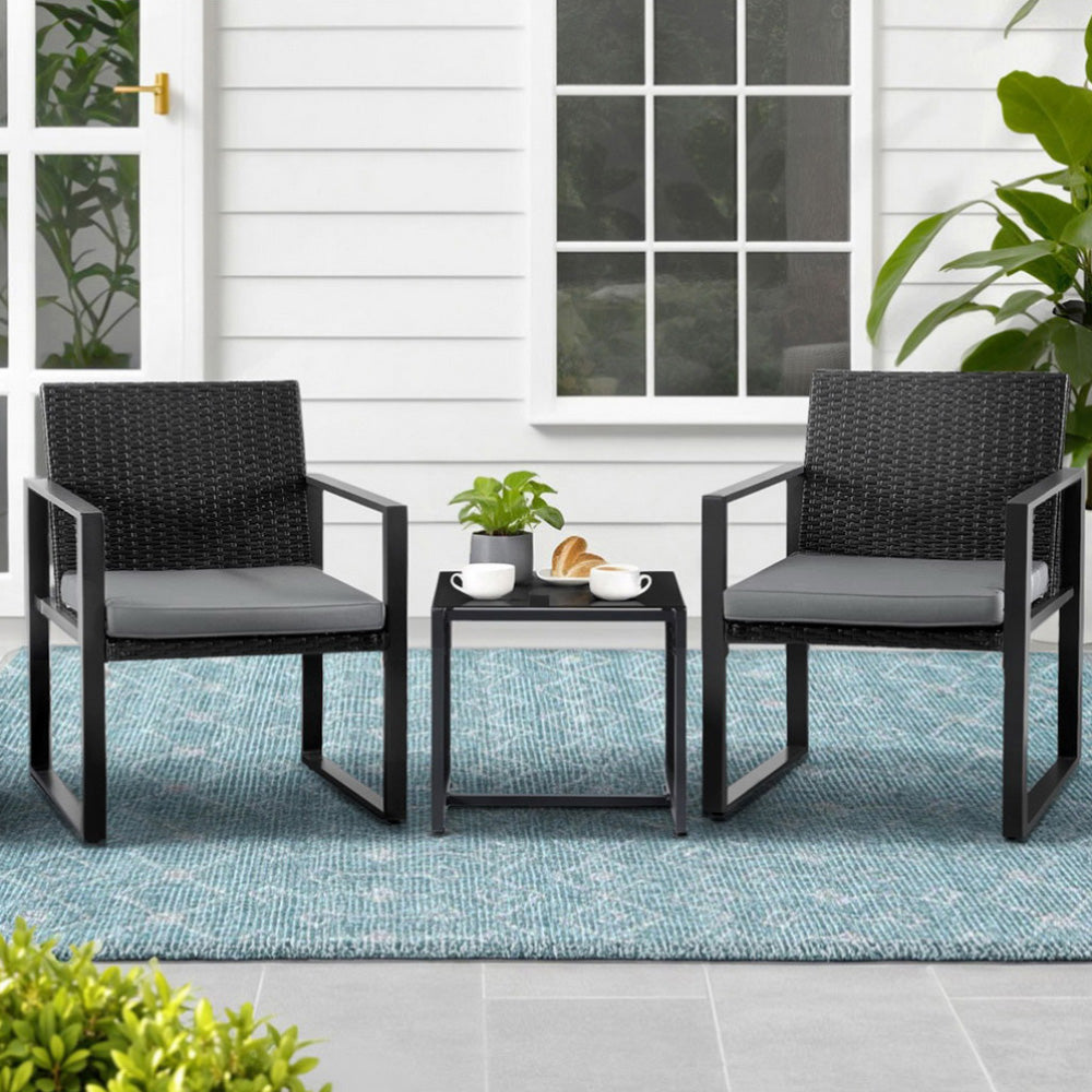 Two black wicker chairs with gray cushions and a matching side table on a patio.
