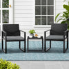 Two black wicker chairs with gray cushions and a matching side table on a patio.