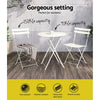 A Gardeon 3PC Outdoor Bistro Set consisting of a folding Steel Table and two folding Chairs in White, showing its weight capacities and set on a wooden floor in front of a tiled wall and some plants in the background.