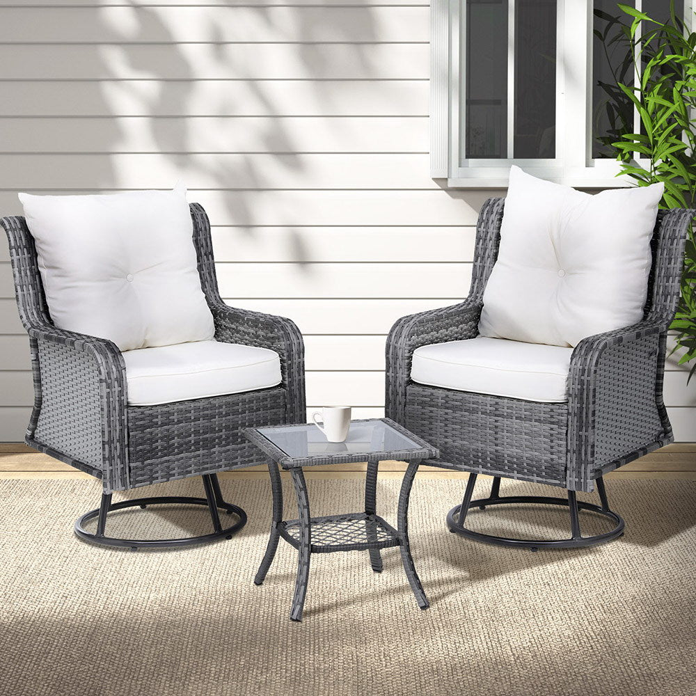 A 3-piece outdoor furniture set featuring a table and two chairs with grey weave pattern and white cushions, in an outdoor patio setting on wood decking with beige colour floor rug set in front of a wall and window with a plant to the side.