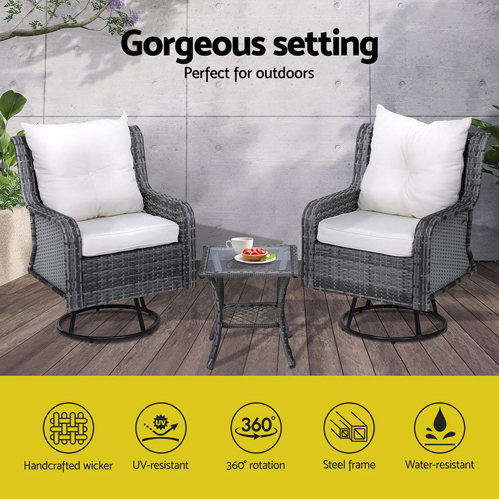 A 3-piece outdoor furniture set featuring a table with a cup and bowl of salad and two chairs with grey weave pattern and white cushions, in an outdoor patio setting on a wood decking in front of a wall with plants to the side.