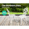 Two white chairs with rose design, set on a wooden decking in front of a grass and greenery in the backdrop.