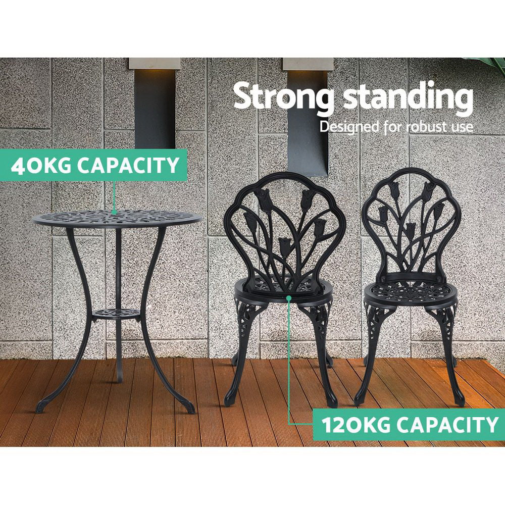 A black Gardeon bistro set including two chairs and a round table, made of cast aluminum with tulip patterns, set on a laminated wood floor before a grey tiled wall, one chair facing forward and one facing backwards, shows the weight capacity being 40kg for the table and 120kg for the chairs.