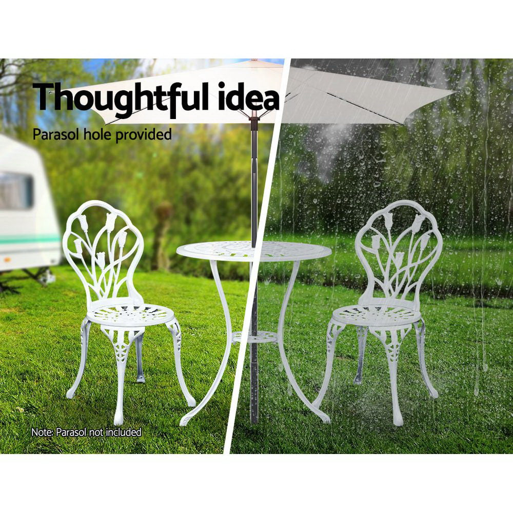 A white Gardeon bistro set including two chairs and a round table, made of cast aluminum with tulip designs, set on a grass and trees in the backdrop. The image is split into two showcasing the parasol hole holding a parasol in the middle of the table, half image in the sunshine offering shade and the other half in the rain also offering cover.